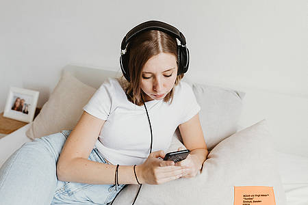 Frau hört zuhause Musik mit einem Kopfhörer über ein Smartphone