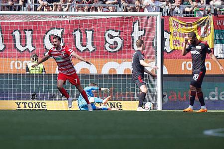 Augsburgs Dion Drena Beljo (l) jubelt nach seinem Tor zum 1:0, der Berliner Torwart Frederik Rönnow (M) schaut dem Ball im Netz nach.