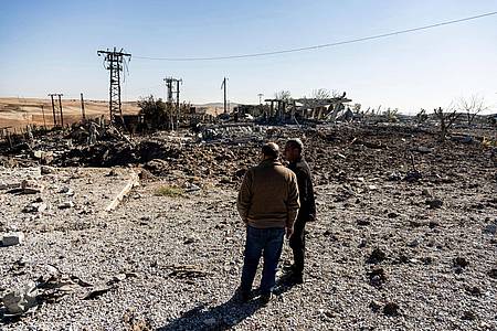 Zwei Männer begutachten Schäden in einem Gebiet um ein Elektrizitätswerk nach türkischen Luftangriffen.