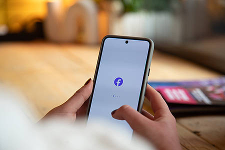 Hände mit Smartphone in der Hand. In der Mitte das Facebook Logo.