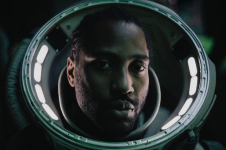 Der Hauptprotagonist von The Creator auf Netflix steht im Raum-Anzug vor verschwommenen Lichtern.