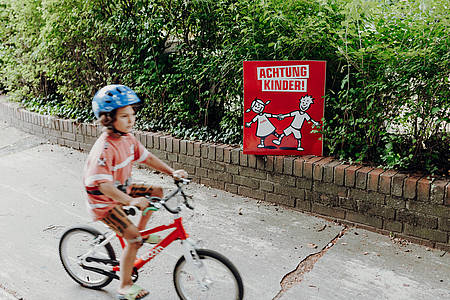 Junge mit Fahrrad neben Achtung Kinder-Plakat